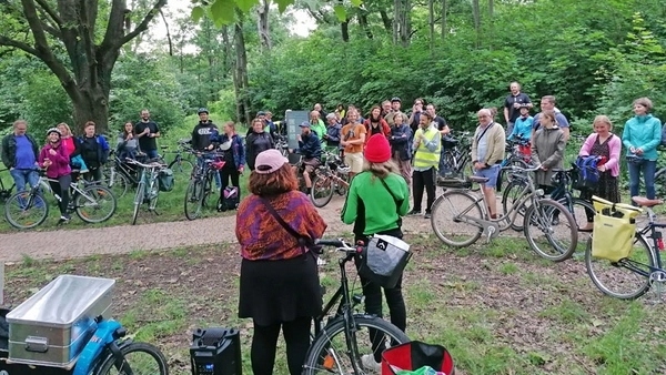 Die Lesebühne bei ihrer Radtour. Zu sehen sind Marsha und Franzi von hinten, die vor einem Publikum in der Natur performen.